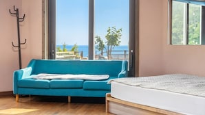 Une pièce avec un canapé bleu, un lit, un porte-manteau et une vue sur la mer.