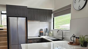 Una cocina moderna con un refrigerador de acero inoxidable, una isla grande con taburetes de bar, una ventana con vistas y un reloj de pared.
