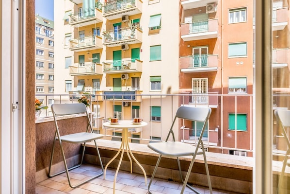 Ein Balkon mit zwei Stühlen und einem kleinen Tisch, mit Blick auf ein mehrgeschossiges Gebäude mit Balkonen und Fenstern.