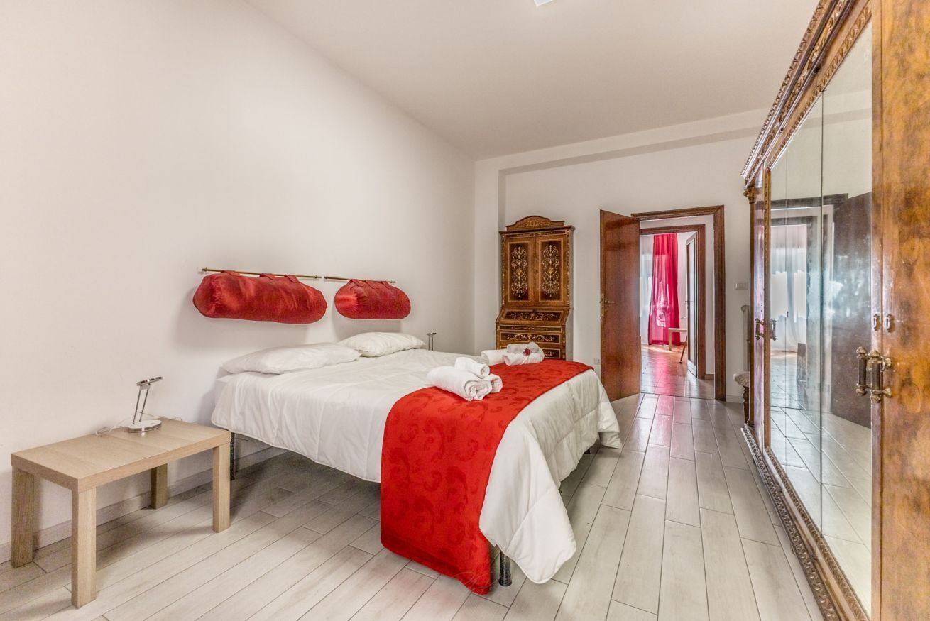 A bedroom with a bed, bedside table, wardrobe, and a mirror.