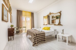 Ein Schlafzimmer mit Bett, Nachttisch, Sessel, Schreibtisch, Spiegel und Vorhängen.