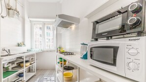 Et lille køkken med en Kooper mikrobølgeovn, en gasblus og hvide skabe.