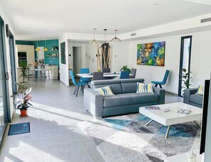 A modern living room with a grey sofa, blue chairs, a white coffee table, and a dining area in the background. - Contemporary villa in Aix-en-Provence vineyards (Le Puy-Sainte-Réparade)
