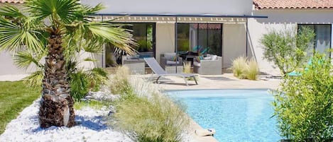 Una casa moderna con piscina, zona de estar exterior y una palmera.