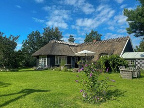 Ein Haus mit einem Strohdach, einem Garten und Sitzgelegenheiten im Freien.