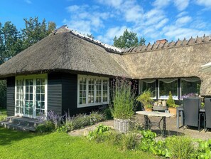 Ein reetgedecktes Häuschen mit Garten, Tisch und Gartenmöbeln.
