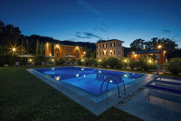 A swimming pool with lounge chairs, a well-lit building, and a clear night sky. - Beautiful apartment near Lucca with pool (Capannori)