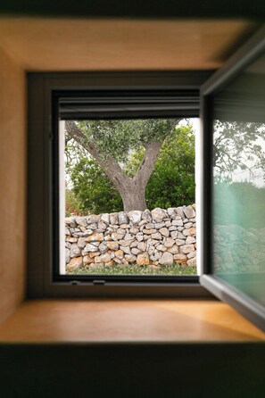 A window with a view of a tree and a stone wall. - Traditional Puglian trullo (Ostuni)