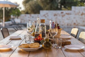 A wooden table set for a meal outdoors with wine glasses, a bottle, and a bowl of fruit. - Traditional Puglian trullo (Ostuni)