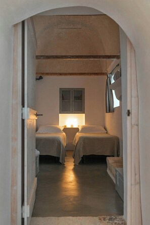 A narrow hallway leading to two beds with bedside tables, a window, and a door. - Traditional Puglian trullo (Ostuni)