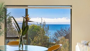 Ein Zimmer mit großem Fenster und Meerblick, einem Glastisch sowie zwei Stühlen.