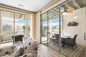 Ein Zimmer mit einer Schiebetür zu einer Außenveranda, die einen Tisch und Stühle, einen Deckenventilator und ein dekoratives Wandelement bietet.