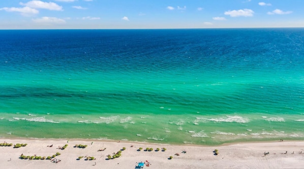Ein Strand mit klarem türkisblauem Wasser, sandigem Ufer und einigen Strandsonnenschirmen.