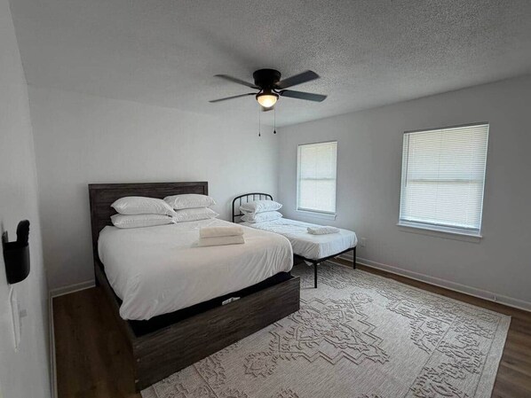 A bedroom with a bed, a bedside table, a ceiling fan, and two windows with blinds. - 2BR 1.5BA New Condo Near Hospitals - Sleeps 5 (Saint Andrews)