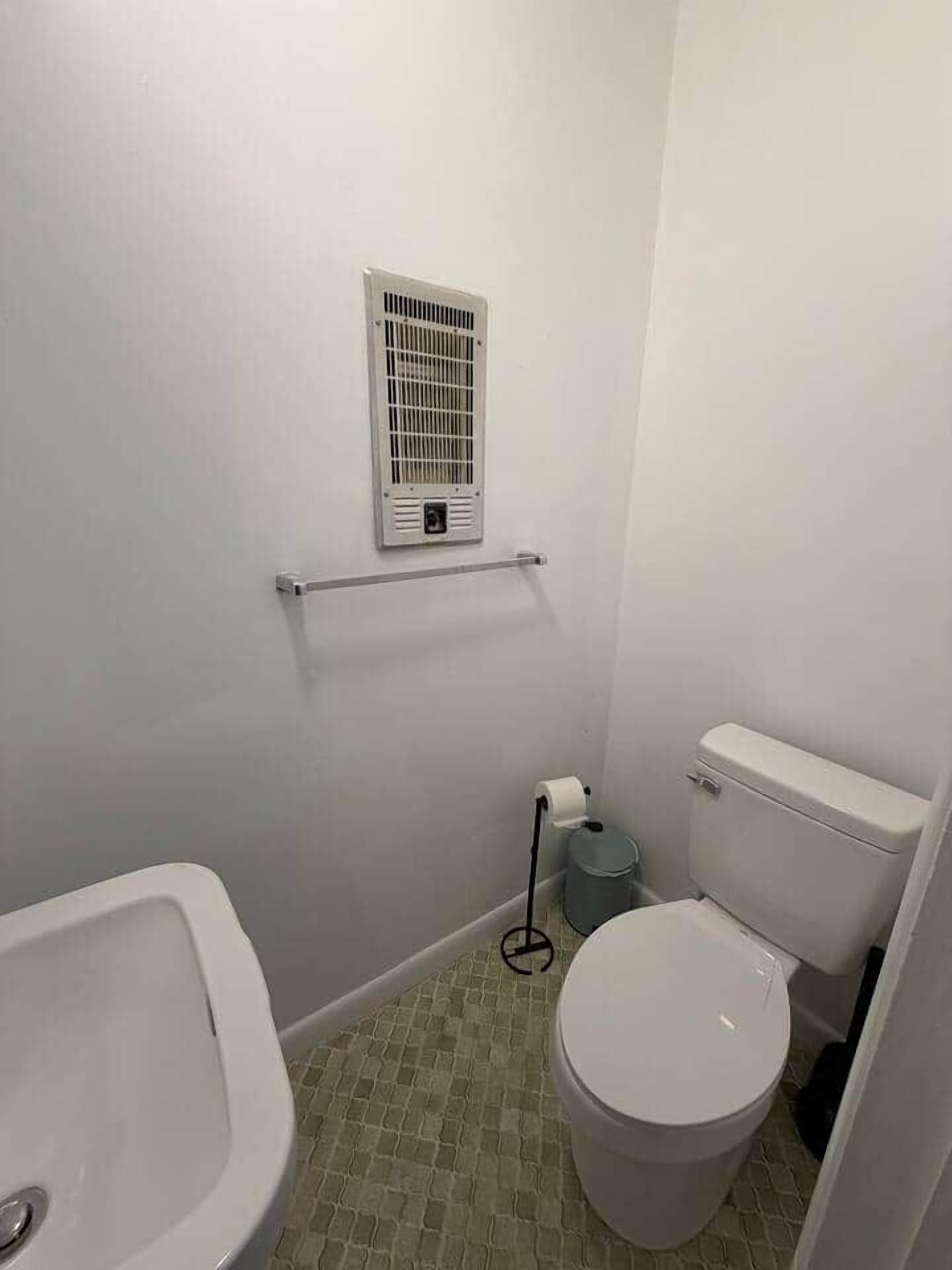 Een compacte badkamer met toilet, wastafel en een ventilatie-unit aan de muur.