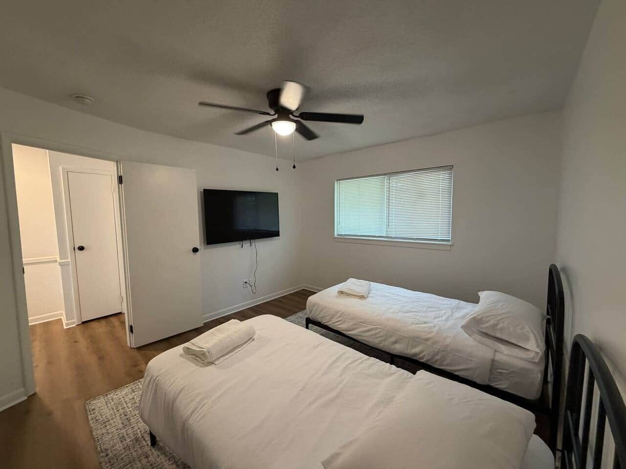 A bedroom with two beds, a ceiling fan, a TV, and a window.