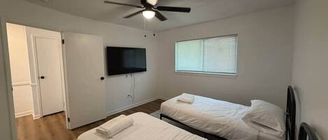 A bedroom with two beds, a ceiling fan, a TV, and a window.