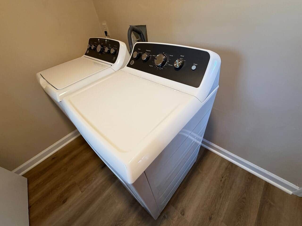 Een compact was- en droogcombinatie, gemonteerd aan de muur, in een wasserij met een houten vloer.