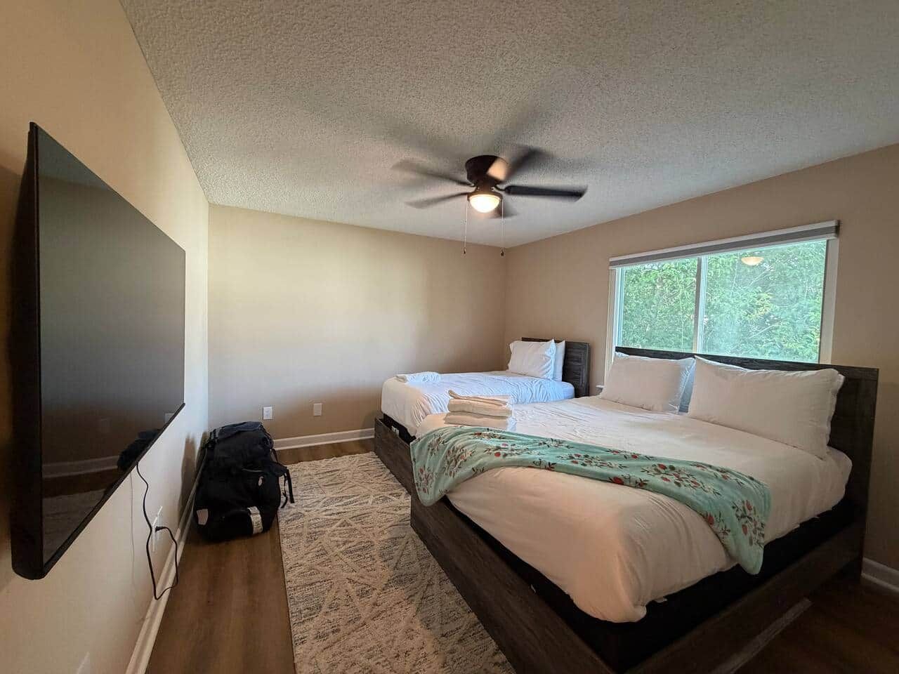 A bedroom with a bed, a ceiling fan, a TV, and a window.