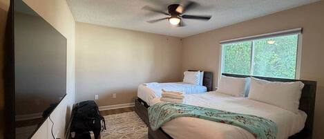 A bedroom with a bed, a ceiling fan, a TV, and a window.