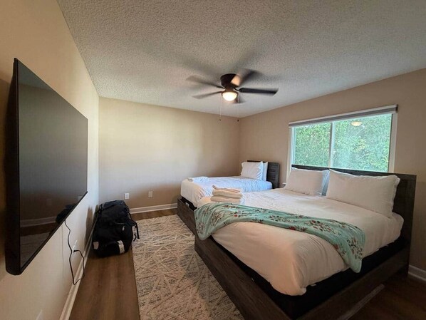 Quarto com cama, ventoinha no teto, televisão e janela.