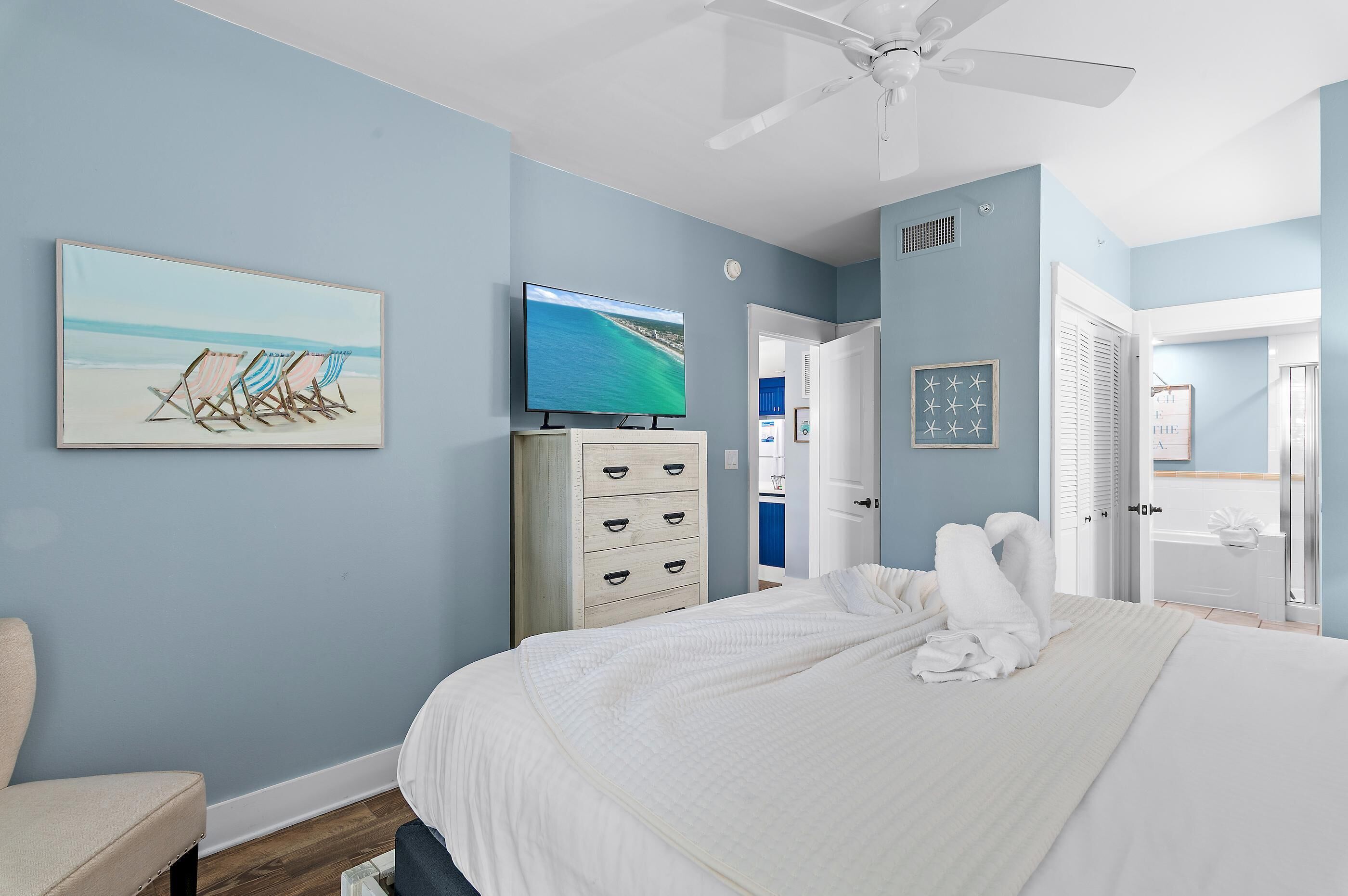 A bedroom with a bed, a TV, a dresser, and a door leading to a bathroom.