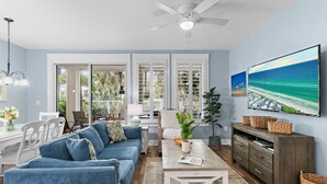 A living room with a sofa, coffee table, TV, and a view of the ocean through large windows. - Pilot House 322 (Miramar Beach)