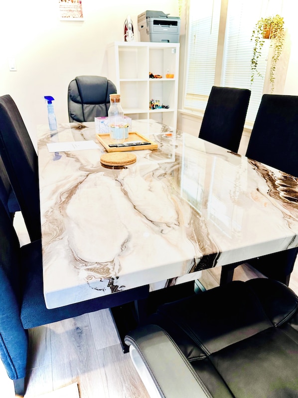 Una mesa de conferencias con acabado de mármol, rodeada de sillas negras, en una sala con un estante blanco e impresora en la pared.