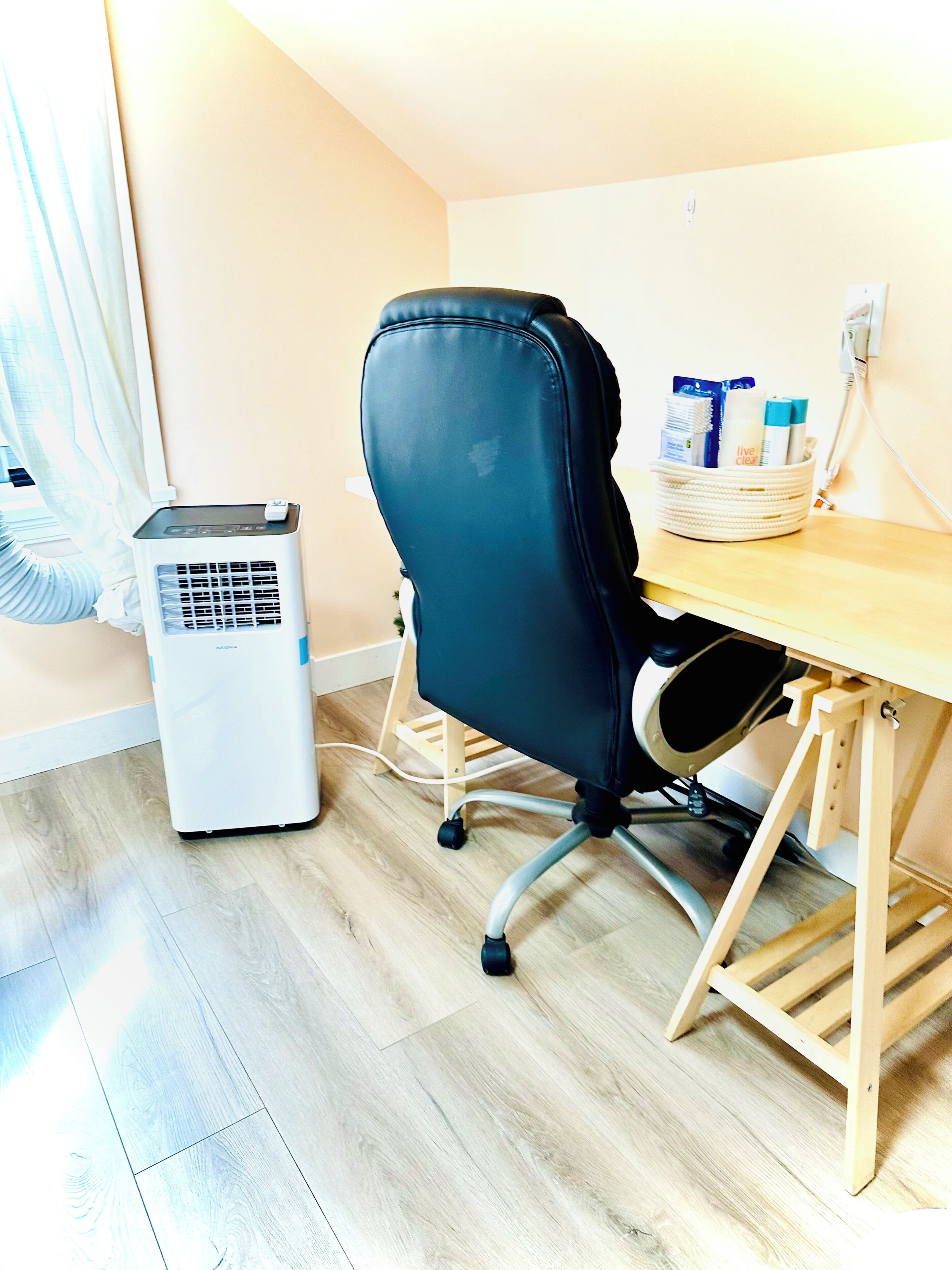 Quarto com escrivaninha de madeira, cadeira de escritório preta, ar condicionado branco e tomada na parede.