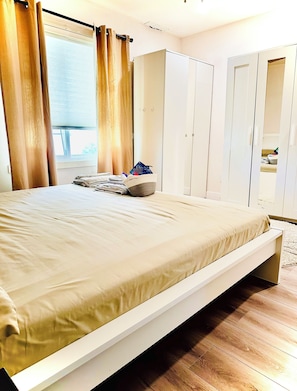 Un dormitorio con cama, armario y ventana con cortinas.