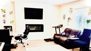 Una sala de estar con una televisión de pantalla plana, un sofá de cuero, un sillón azul, un piano y una mesa de centro.