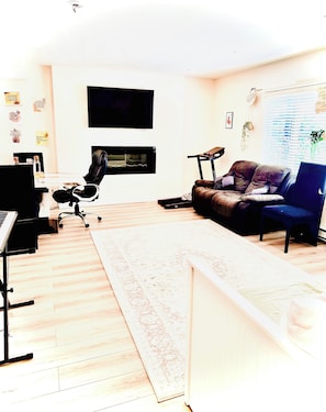 Una sala de estar con una televisión de pantalla plana, un sofá de cuero, un sillón azul, un piano y una mesa de centro.