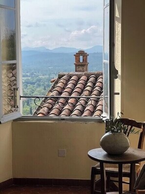 A room with a view of a tiled roof and mountains, a small table with a vase, and a chair. - Village house with valley view in Tourrettes (Tourrettes)