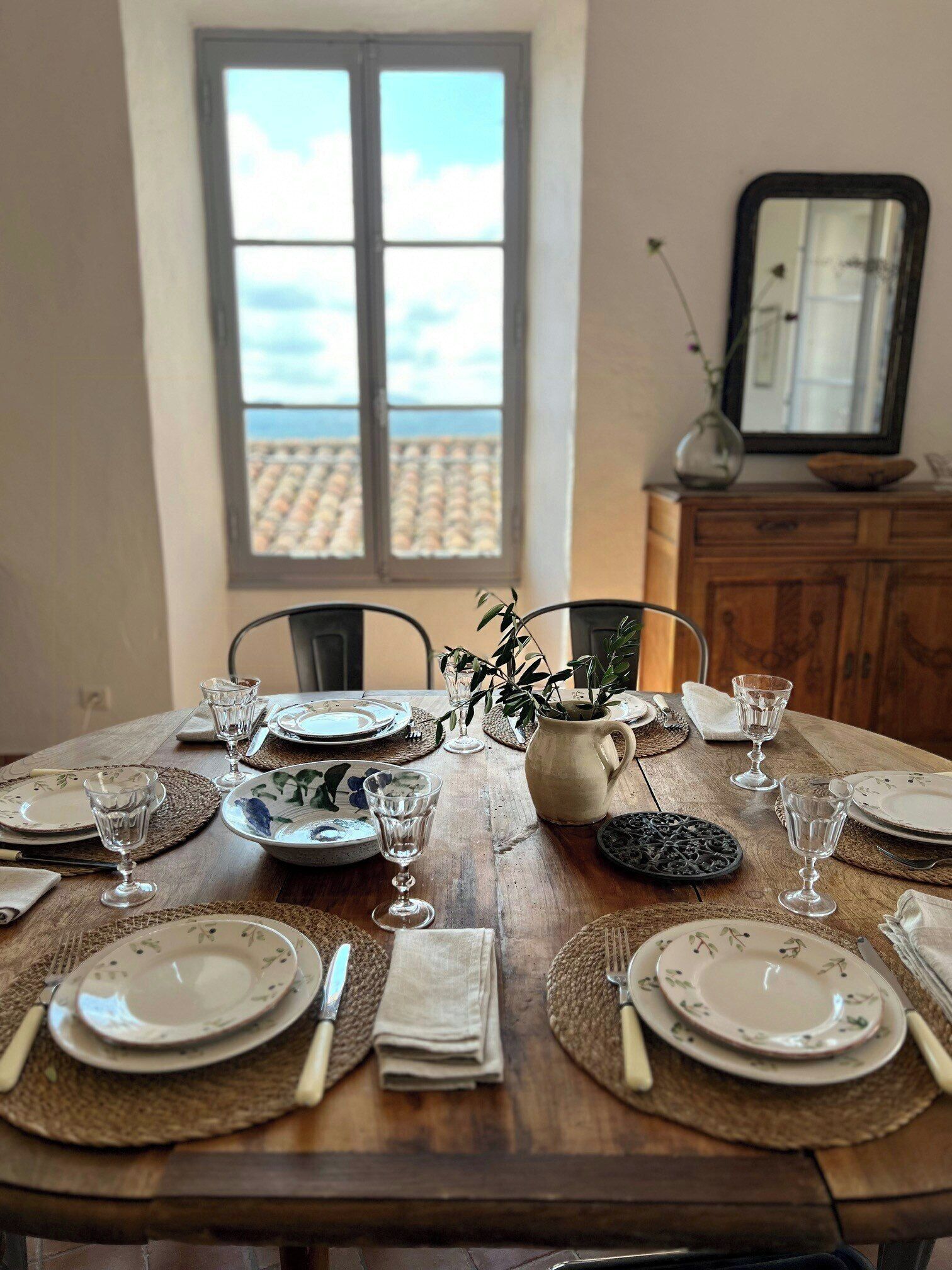 Una tavola imbandita con piatti, bicchieri e una caraffa, con vista sul cielo attraverso una finestra.