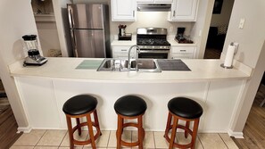 A kitchen with a stainless steel refrigerator, a stove, a sink, and three wooden stools. - Spacious 3BR 2BA near Airport, Mercedes Benz Stadium, Dwntwn ATL, GICC, Trilith (Union City)