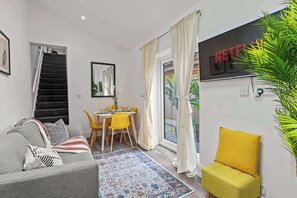 Una sala de estar moderna con un sofá, una silla amarilla, una mesa de comedor con sillas amarillas, una escalera y un ventanal con cortinas.