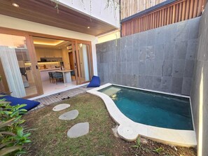 Ein moderner Poolbereich im Freien mit einer Steinwand, einem Holzboden und einer Glastür, die zu einer Küche führt.