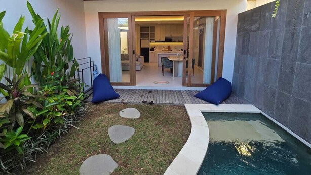 Ein moderner Außenbereich mit Pool, einer Holzterrasse und Blick auf eine Küche und ein Wohnbereich.