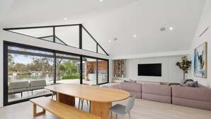 Un salon moderne avec une grande table à manger, un canapé, un téléviseur et une vue sur une structure en briques à l’extérieur.