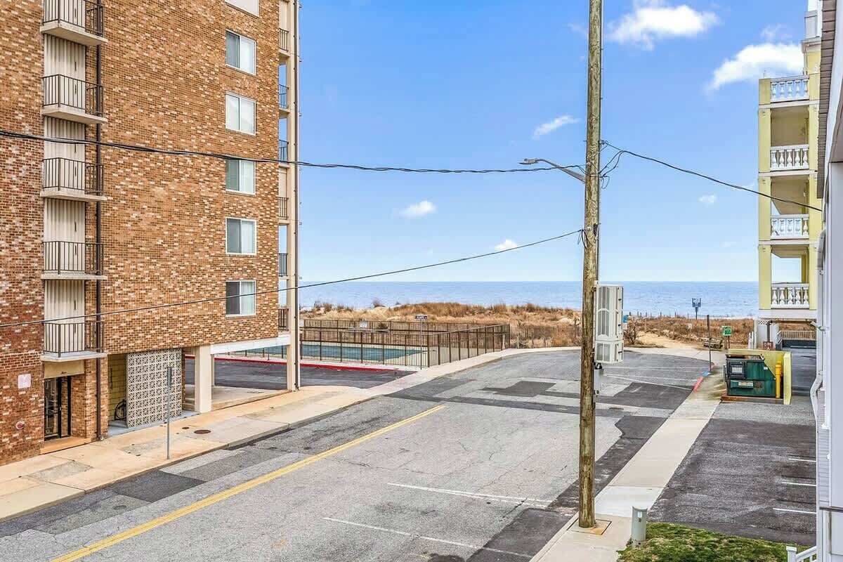 A multi-story residential building with balconies, a parking lot, and a view of the beach.