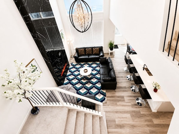 En modern inredning med en trappa, en svart lädersoffa, en mönstrad matta och en kristallkrona.