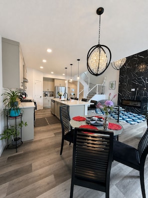 Een moderne keuken met een centraal eiland, een eetgedeelte met een ronde tafel, en een accentmuur van zwart marmer.