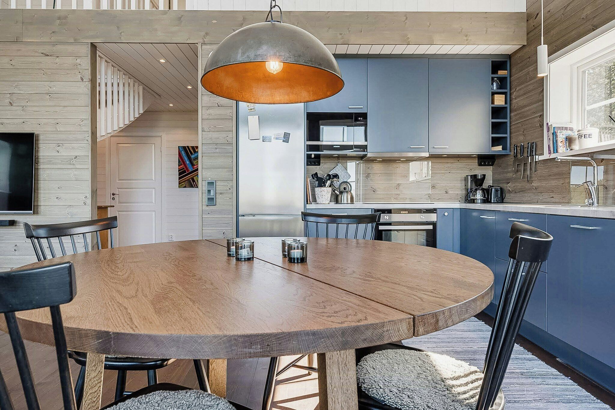 A modern kitchen with blue cabinets, a wooden dining table, and a hanging light fixture.