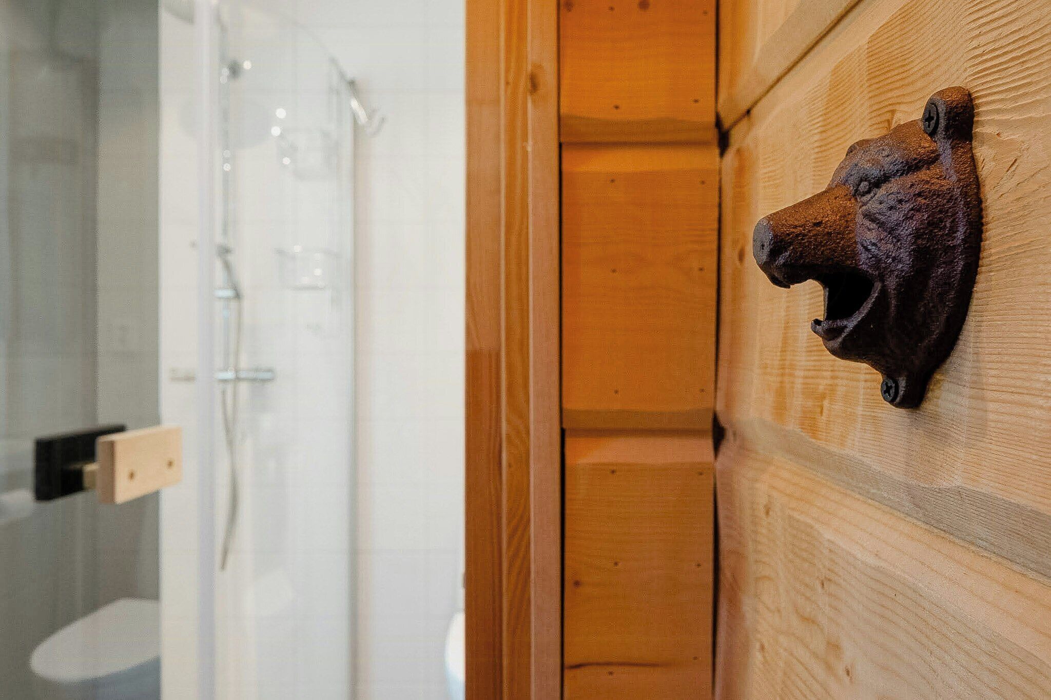 A wooden wall with a bear head decoration, a glass shower enclosure, and a wooden door.