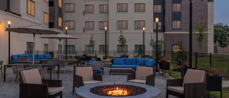Un patio con mobiliario exterior, una fogata y un edificio con varias ventanas.