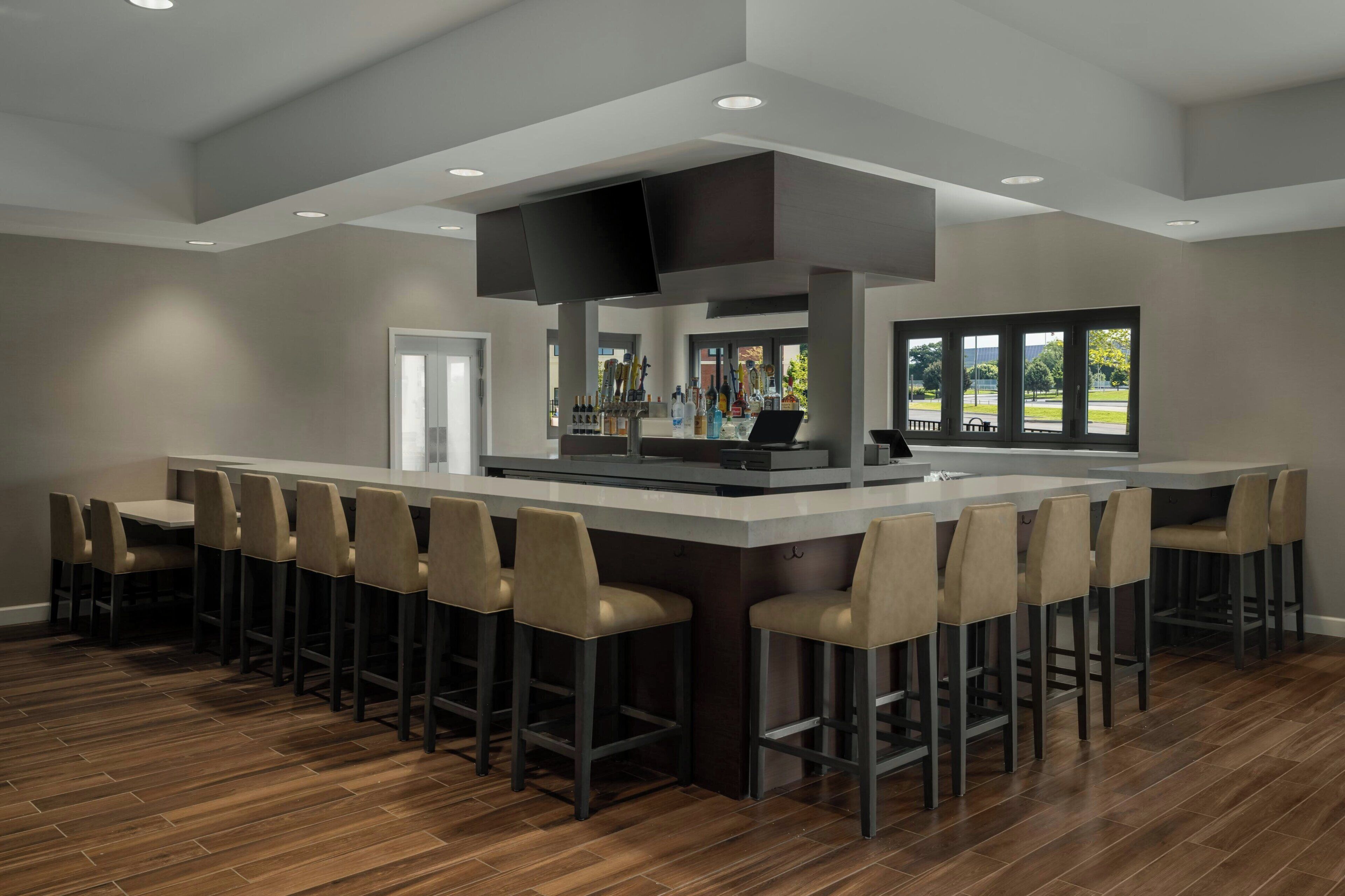 A modern bar area with a central island, bar stools, and a large window providing a view.
