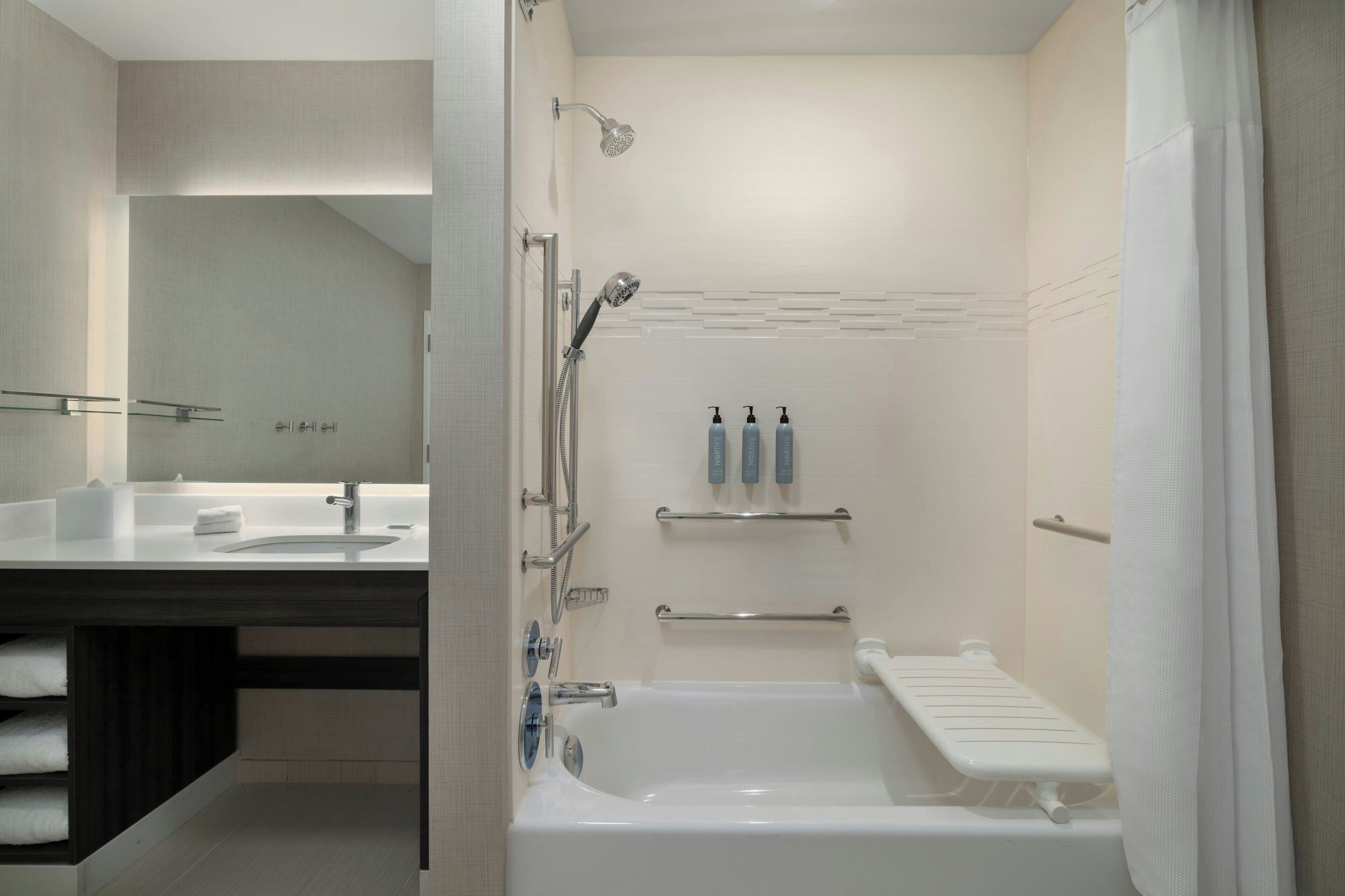 A modern bathroom with a bathtub, a shower, a vanity with a mirror, and a towel rack.