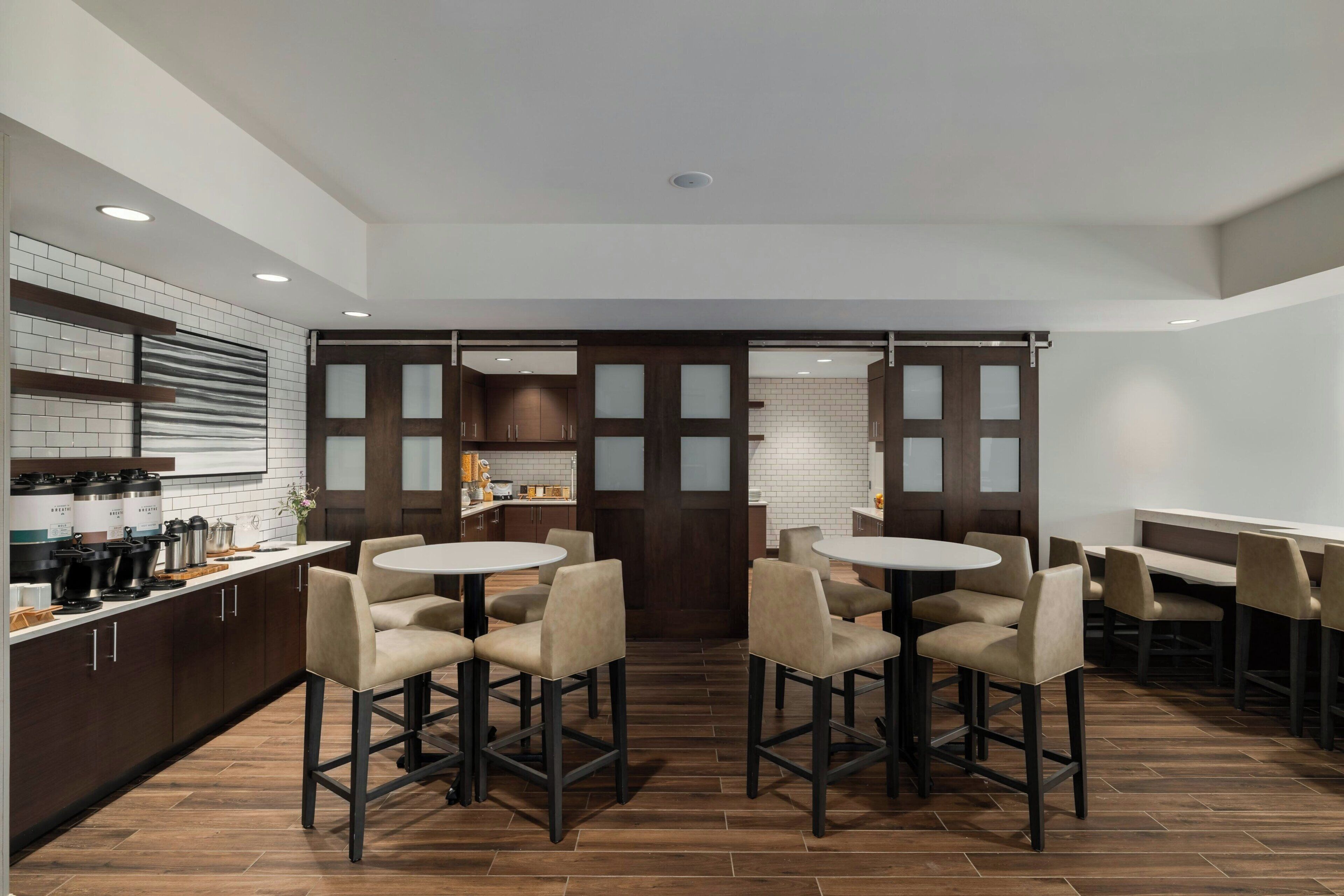 A modern kitchen with a central island, bar stools, and a dining area with tables and chairs.