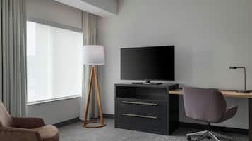 A hotel room with a desk, chair, television, lamp, and a large window with curtains.