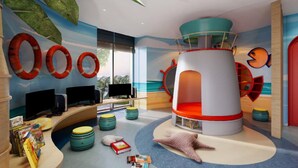 Espaço infantil com uma estrutura cilíndrica central, vários monitores sobre uma mesa e diversas opções de assentos coloridos.